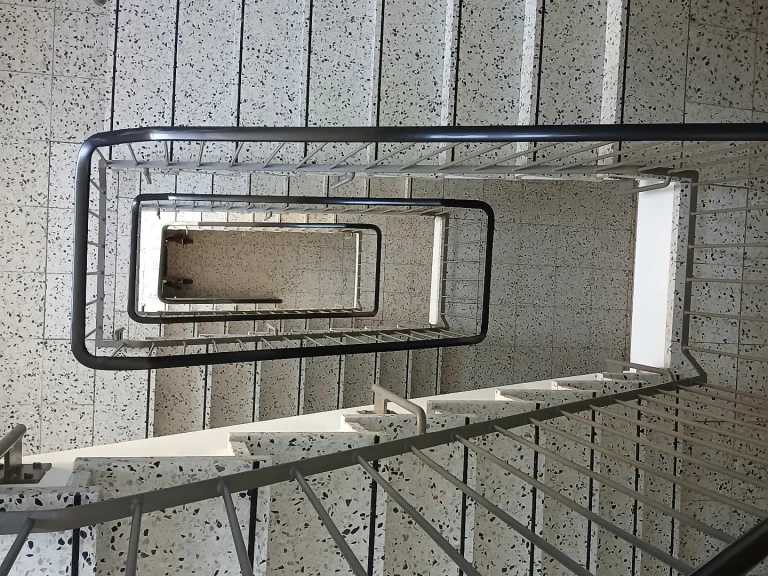Treppenhausreinigung Hannover Ein spiralförmiges Treppenhaus mit grauem Geländer und hellen Stufen.